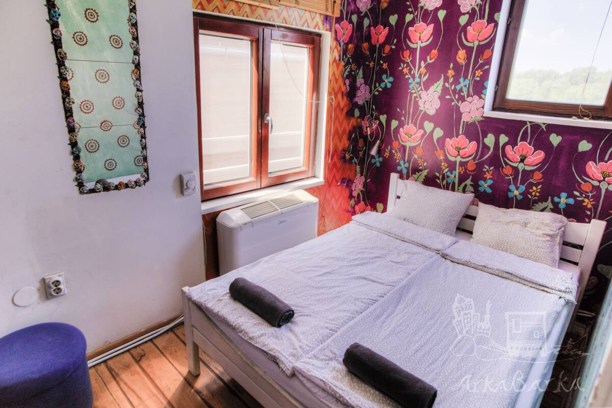 A bedroom with a bed, a window, a radiator, and a wall with floral wallpaper.