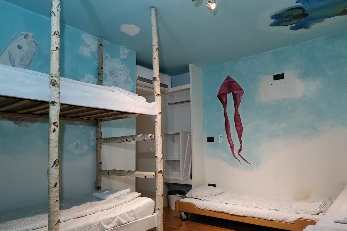 A bunk bed room with a bunk bed on the left and a single bed on the right. There is a wardrobe with a mirror and a red kite decoration on the wall.