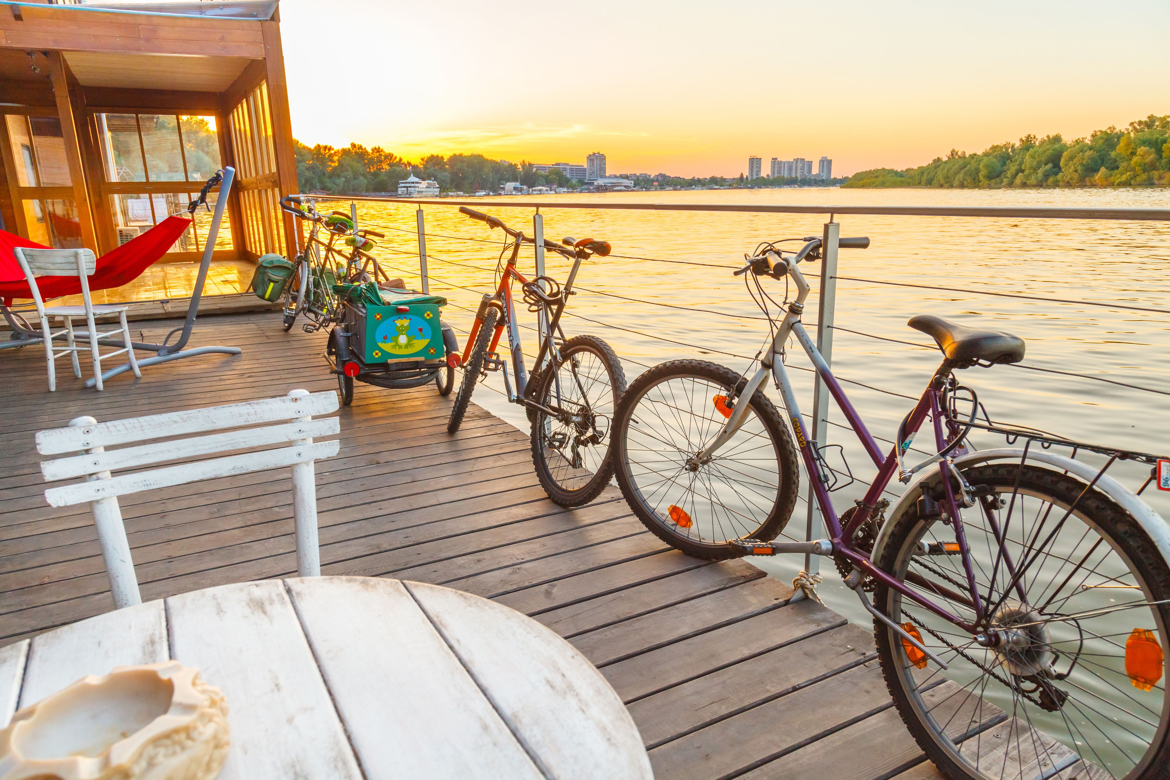 A wooden deck with bicycles, a hammock, and a bench overlooking a body of water.