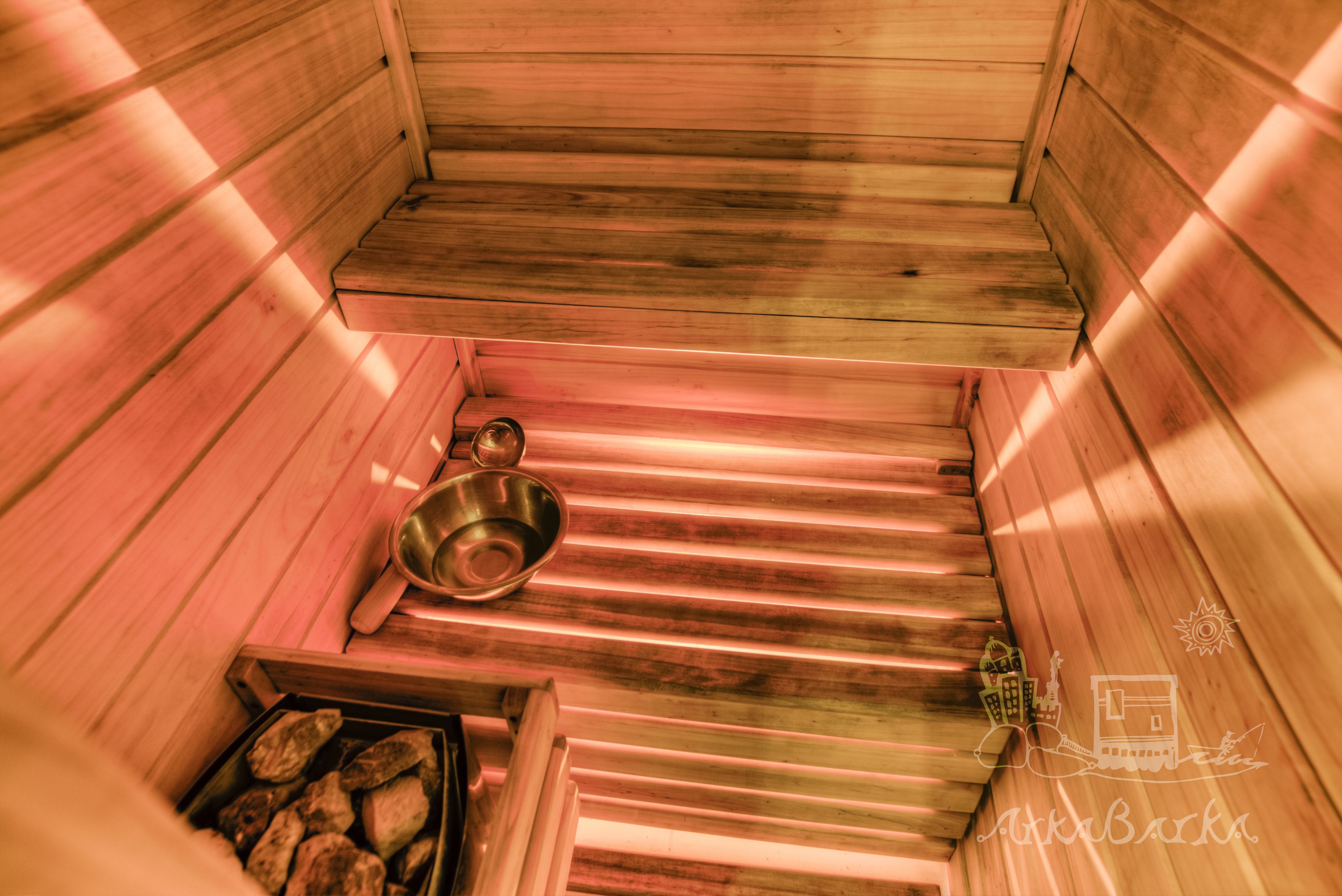 Een sauna met houten banken, een metalen wasbak en een schaal stenen.