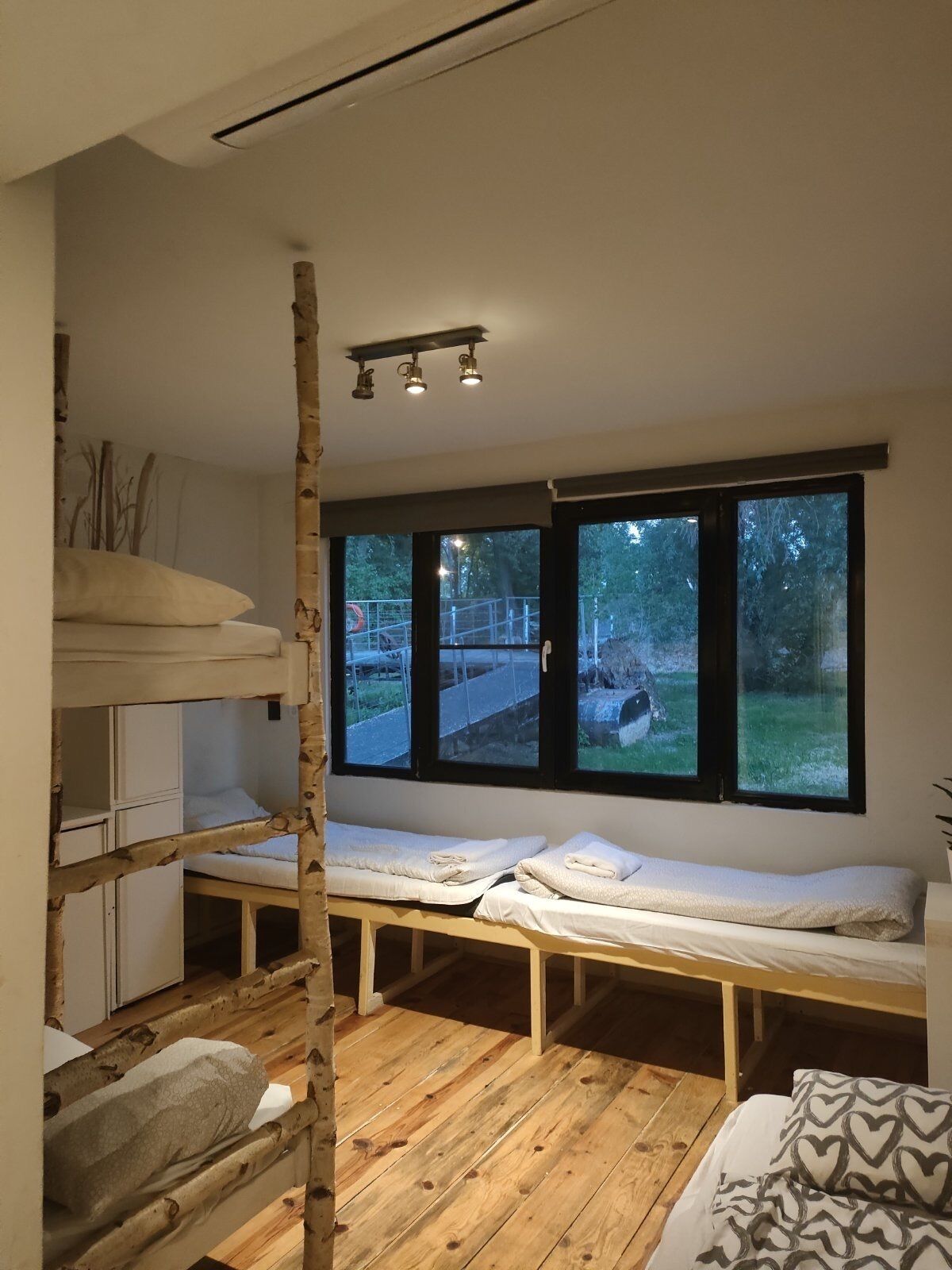 A compact room with bunk beds, a wooden floor, and large windows offering a view of the outdoors.