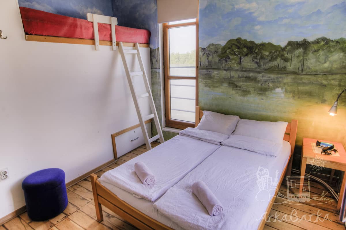 A room with a bed, a ladder, a window, and a mural of a landscape.
