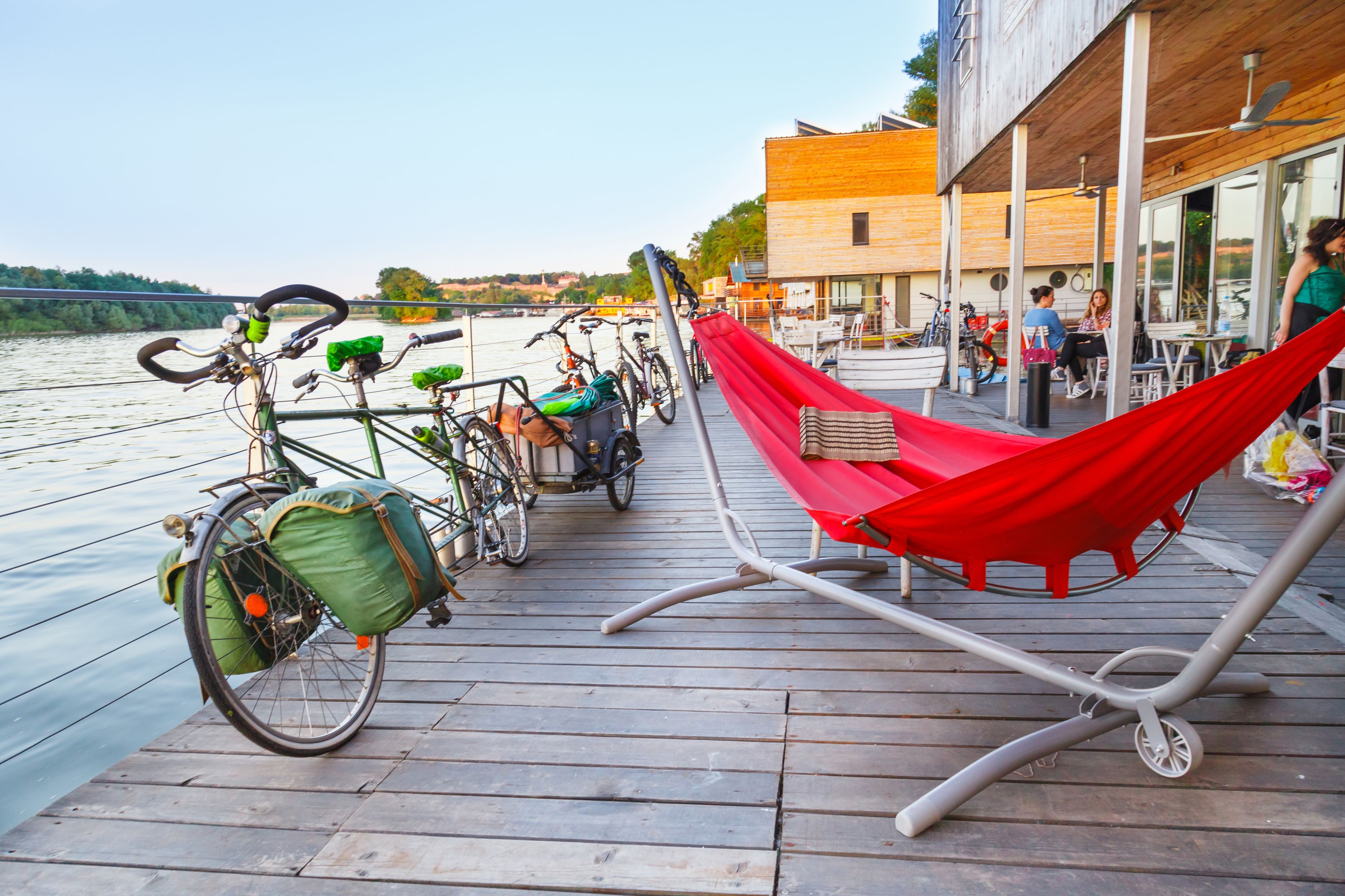 Une terrasse en bois avec des vélos, un hamac rouge et une vue sur l’eau.