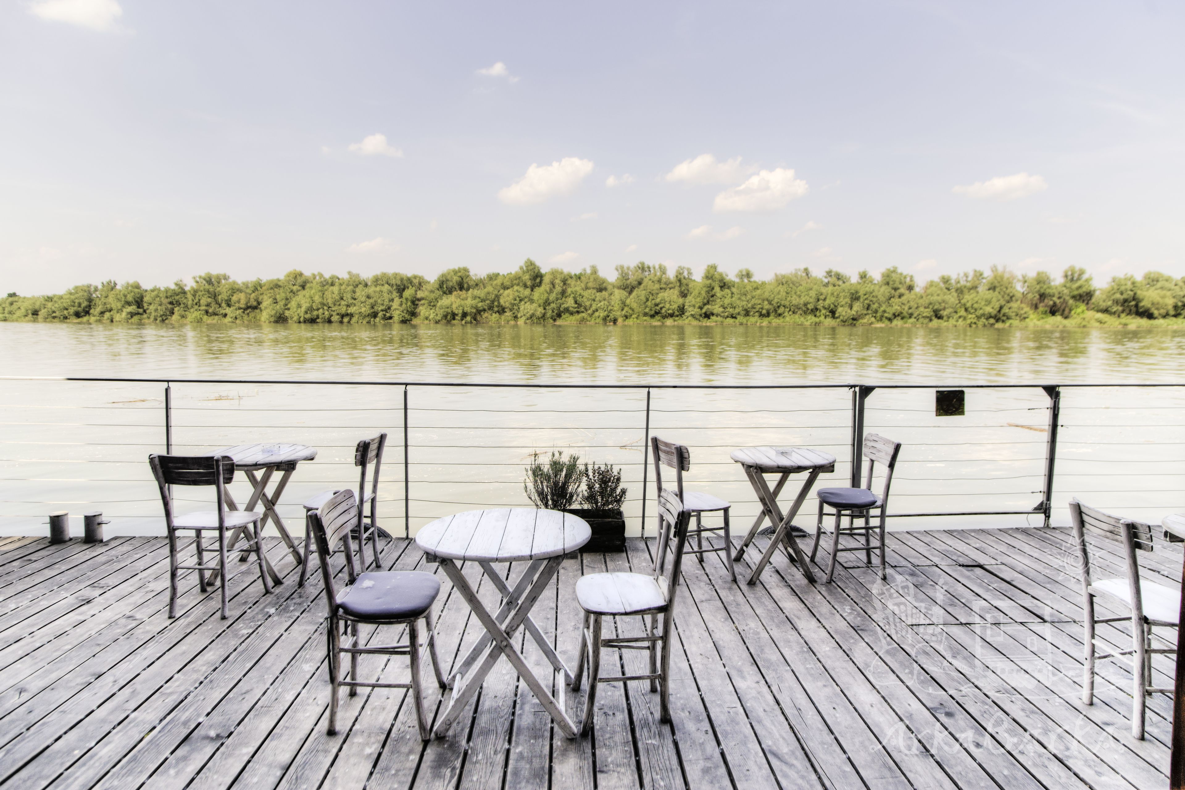 Terraza de madera con mesas y sillas con vista a un río tranquilo.