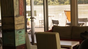 A room with a view of a lake, a sofa, a table, and chairs. - ArkaBarka Floating Hostel and Apartments (Belgrade)