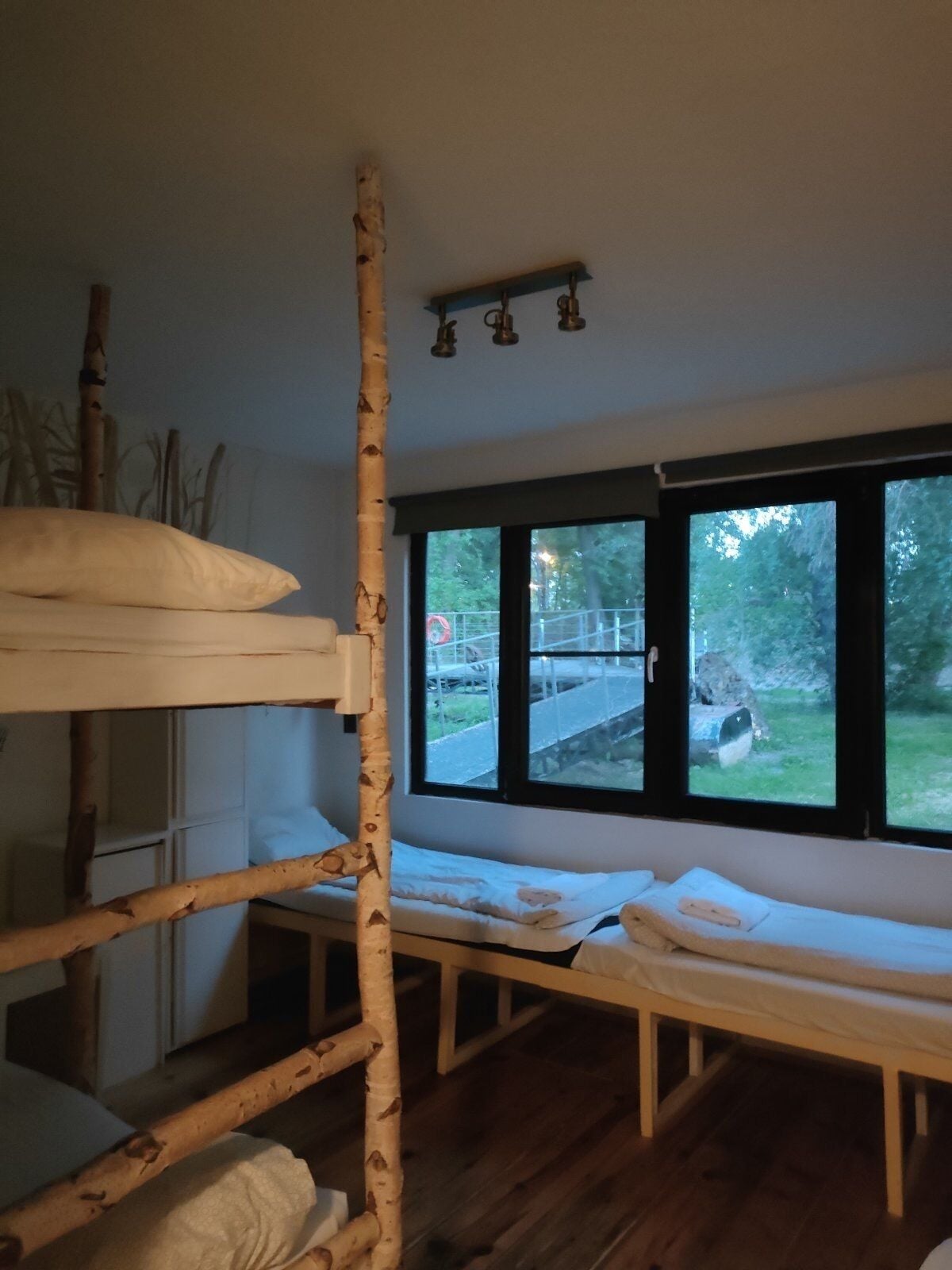 A bunk bed with a ladder, a window with a view of the outdoors, and a small table with a chair.