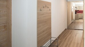 Un pasillo con suelo de madera, un perchero de metal y un espejo que refleja una zona de cocina.