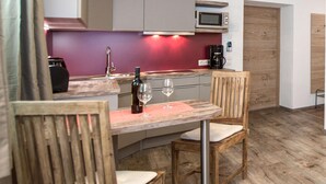 Una cocina con barra de madera, dos sillas, una botella de vino y copas.