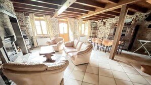 A spacious living area with a stone fireplace, a large beige sofa, and a dining table. - Homerez - Charming House in Lanobre with Garden (Lanobre)