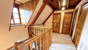 A wooden staircase leading to a loft bedroom with a sloped ceiling and a view of a stone wall. - Homerez - Charming House in Lanobre with Garden (Lanobre)