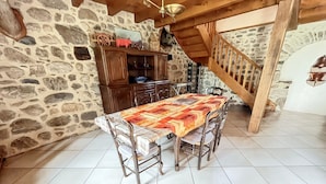 A dining area with a table, chairs, a wooden staircase, and stone walls. - Homerez - Charming House in Lanobre with Garden (Lanobre)