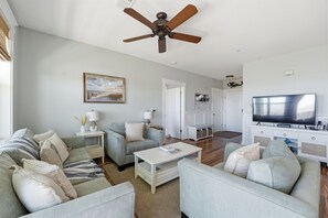 A spacious living room with a ceiling fan, a television, and a painting on the wall. - Knot 4 Sail -Beach Front- Ocean Views- Front Row - 2BD/2BA. Sleeps 6 (Galveston)