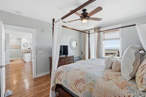 A bedroom with a four-poster bed, a ceiling fan, a large window with a view, and a separate bathroom.