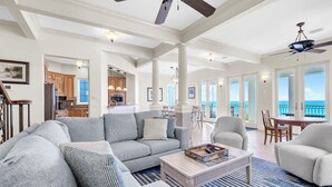 A spacious living room with a gray sofa, a coffee table, and a view of the ocean through large windows.
