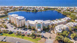 An aerial view of a coastal resort with a large central lake, surrounded by residential buildings and a hotel with a prominent central tower.