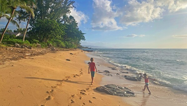 Una playa arenosa con huellas, un niño y un adulto caminando, y vista al océano.
