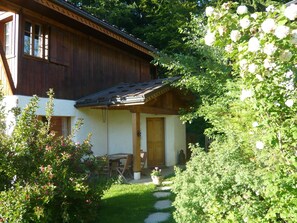Una casa de fusta amb un porxo, un jardí amb pedres apassades i una taula i cadires de fusta.