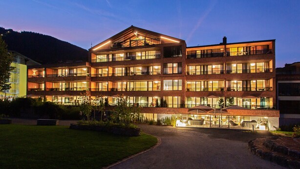 A multi-story hotel with a central atrium, large windows, and a well-lit entrance.