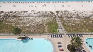 An aerial view of a beach resort with a swimming pool, beach umbrellas, and lounge chairs. - Lighthouse 608 - Great Location on the Gulf-Gulf Shores-Signature Properties (Gulf Shores)