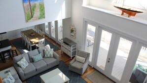 A spacious living area with a gray sofa, a coffee table, and a dining table with chairs. There is a large window providing a view of the outdoors.