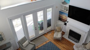 A living room with a fireplace, a television, and a view of the outside deck.