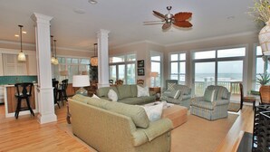 A spacious living room with a large green sofa, a striped armchair, and a ceiling fan. - OCEANFRONT / Sleeps 14 / BISHOPS / POOL / ELEVATOR / SUMMER KITCHEN (Isle of Palms)