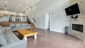 En rummelig stue med en stenvægspejs, et fladskærms-tv ophængt på væggen og en trappe til en etage ovenpå.