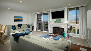 Een woonkamer met een bank, een open haard, een televisie en uitzicht op het strand.