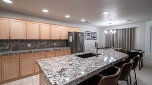 A modern kitchen with granite countertops, wooden cabinets, a stainless steel refrigerator, and a bar area with bar stools. - Spacious Family Condo  Ground Floor, Patio, Pools & Bikes & Fun All YEAR-ROUND  (St George)