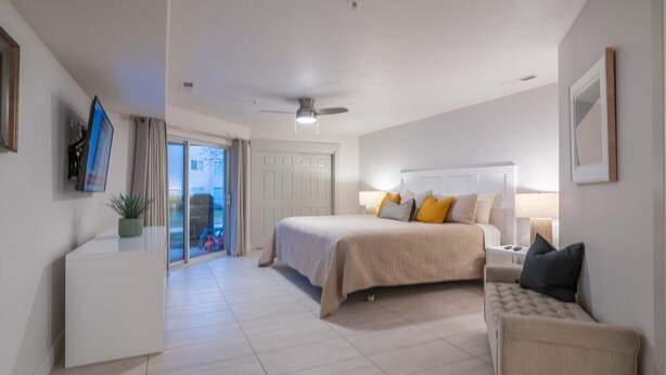 A hotel room with a bed, bedside table, chair, and a view of the outside. - Spacious Family Condo  Ground Floor, Patio, Pools & Bikes & Fun All YEAR-ROUND  (St George)