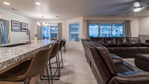 A modern kitchen with a granite countertop, bar stools, and a dining area. There is a leather sofa and a ceiling fan in the living area. - Spacious Family Condo  Ground Floor, Patio, Pools & Bikes & Fun All YEAR-ROUND  (St George)