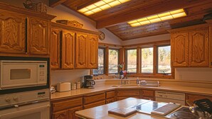 A kitchen with wooden cabinets, a microwave, a coffee maker, and a window with a view of trees. - Amazing property & Shasta views, private lake, dark skies, close to everything (Mt. Shasta)