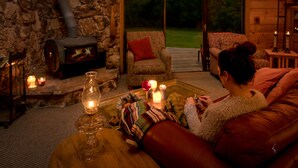 A cozy interior with a stone fireplace, a wooden table with candles, and a red leather couch. - Amazing property & Shasta views, private lake, dark skies, close to everything (Mt. Shasta)