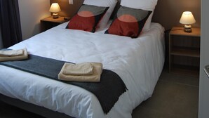 Ein ordentlich bezogenes Bett mit weißen Leinen, zwei Nachttischlampen, ein an der Wand hängendes abstraktes Gemälde und eine Pendelleuchte.