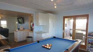 A pool table with balls, a television above it, and a door leading to a balcony. - Last minute special/Ocean Front/ Pool, Pool Table/pet friendly (Nags Head)