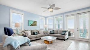 A spacious living room with a ceiling fan, large windows, and a cozy seating area.