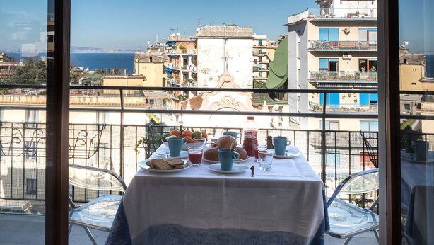 Une table de balcon dressée avec des éléments pour le petit-déjeuner, offrant une vue sur le paysage urbain de la côte.