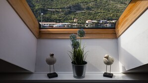 Une fenêtre de toit offrant une vue sur une colline verdoyante et un plan d’eau.