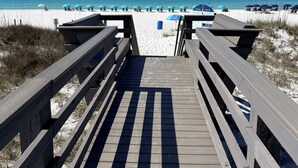 Une promenade en bois menant à une plage où l’on trouve des parasols et des chaises de plage.