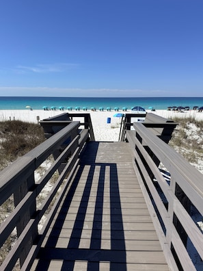 A wooden boardwalk leading to a beach with umbrellas and beach chairs.