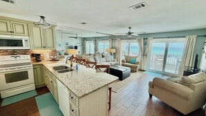Un vaste espace de vie comprenant une cuisine, une grande fenêtre donnant sur l’océan et un balcon avec des sièges d’extérieur.