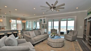 A spacious living room with a large window offering a view of the ocean, a ceiling fan, and a modern kitchen in the background. - OCEANFRONT / Sleeps 16 / BELLA VISTA / POOL / SPA / ELEVATOR / ELEGANT HOME (Isle of Palms)