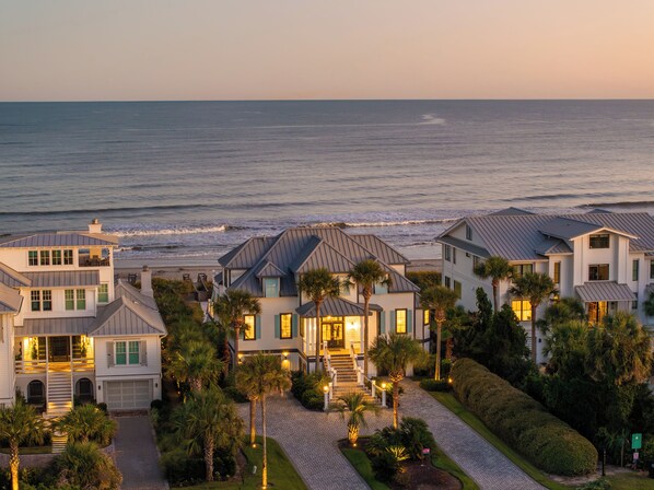 A coastal residential area with houses featuring balconies, a paved driveway, and a view of the ocean.