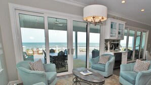 A spacious living area with a view of the beach, featuring light blue armchairs, a coffee table, and a kitchen area with a view. - OCEANFRONT / Sleeps 16 / BELLA VISTA / POOL / SPA / ELEVATOR / ELEGANT HOME (Isle of Palms)