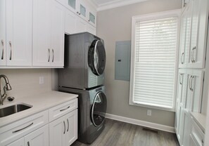 A laundry room with a stacked washer and dryer, a sink, and cabinets.