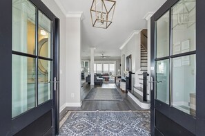 A modern interior with a central hallway leading to a living area, featuring glass doors, a patterned rug, and a ceiling light fixture.