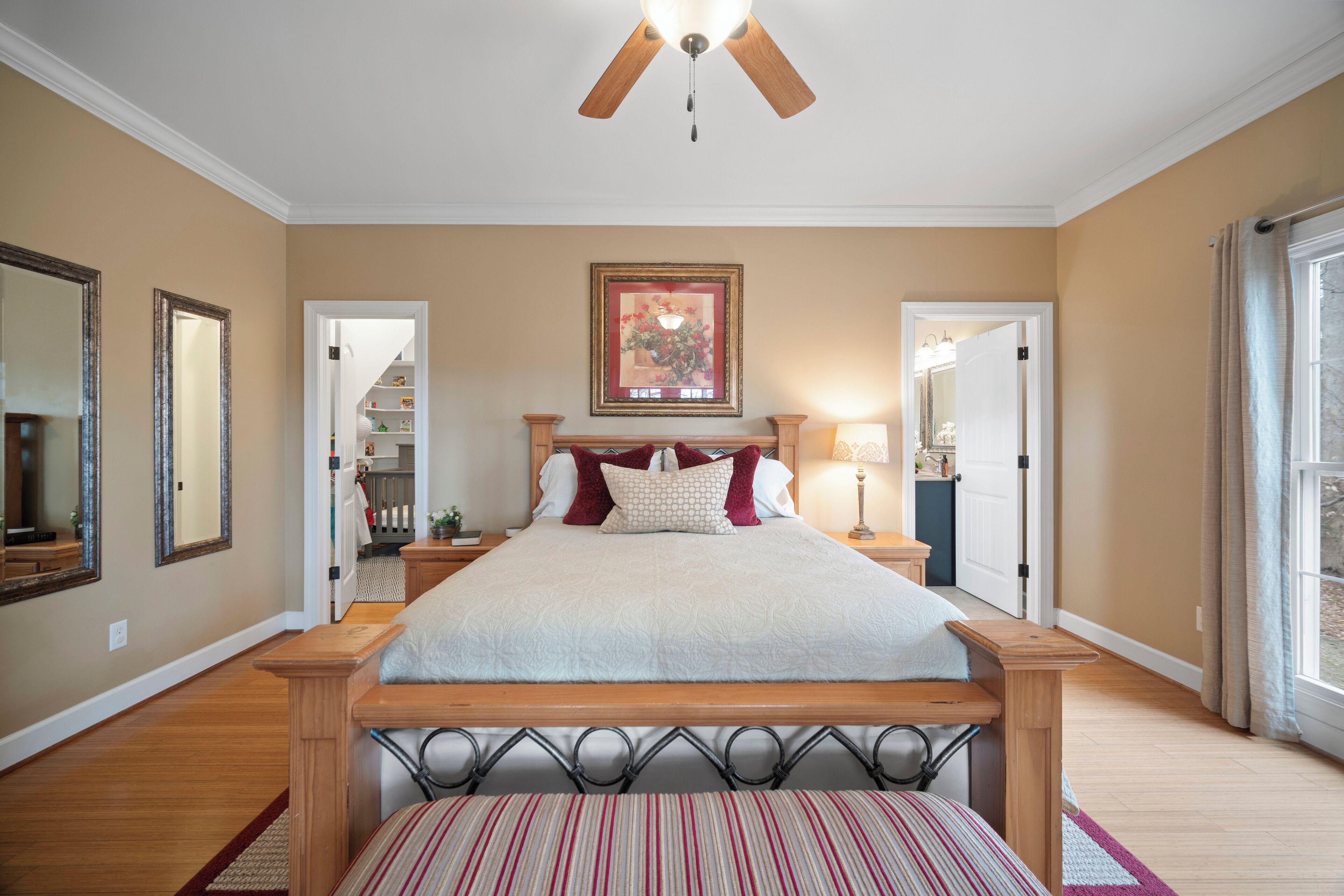 A bedroom with a wooden bed frame, a ceiling fan, a large framed picture, and a nightstand with a lamp.
