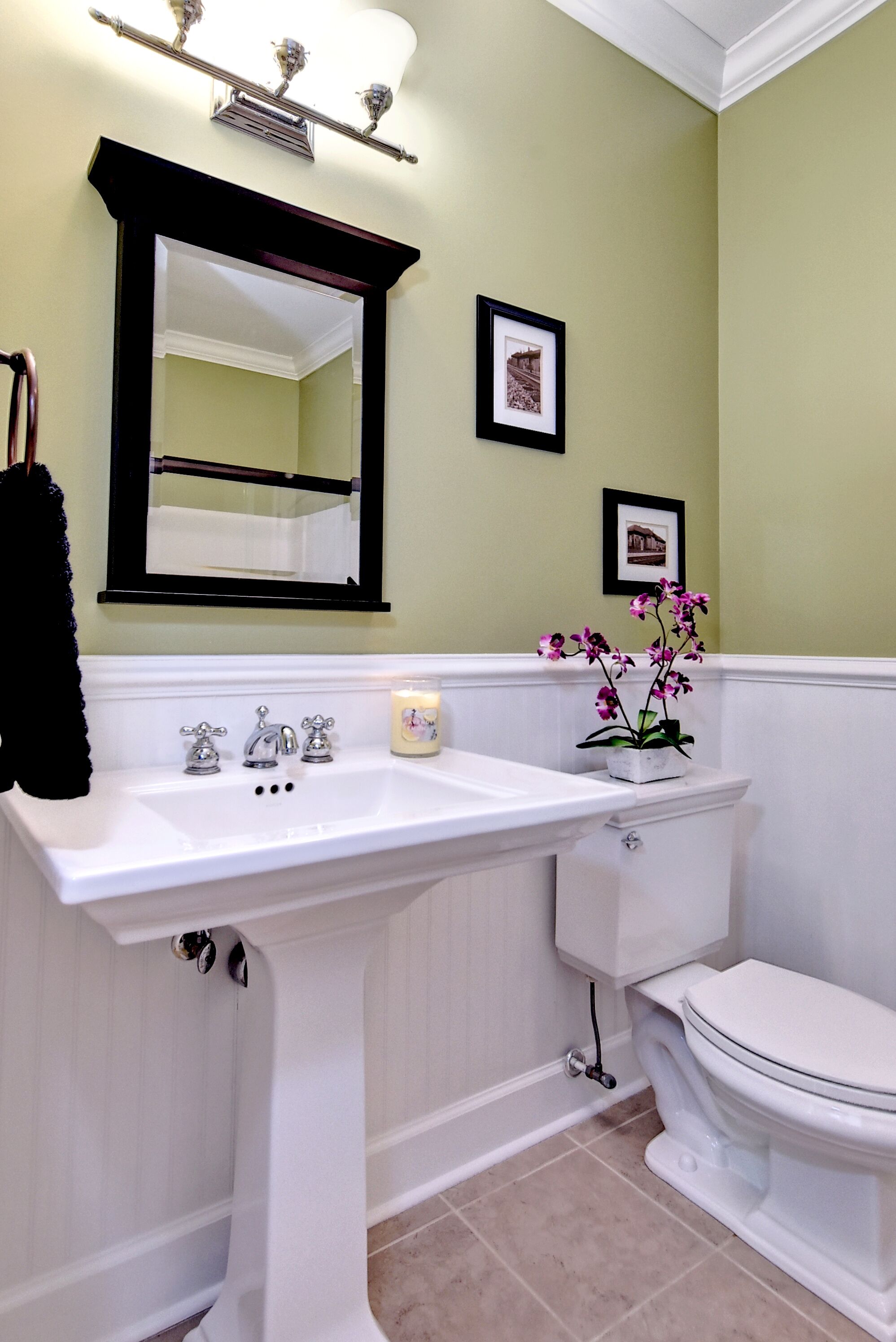 A bathroom with a white sink, a toilet, a framed picture on the wall, and a small potted orchid on the sink.