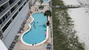 A hotel with a large pool surrounded by lounge chairs and umbrellas, adjacent to a sandy beach.