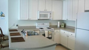 A kitchen with white cabinets, a microwave, a stove, a refrigerator, and a sink.